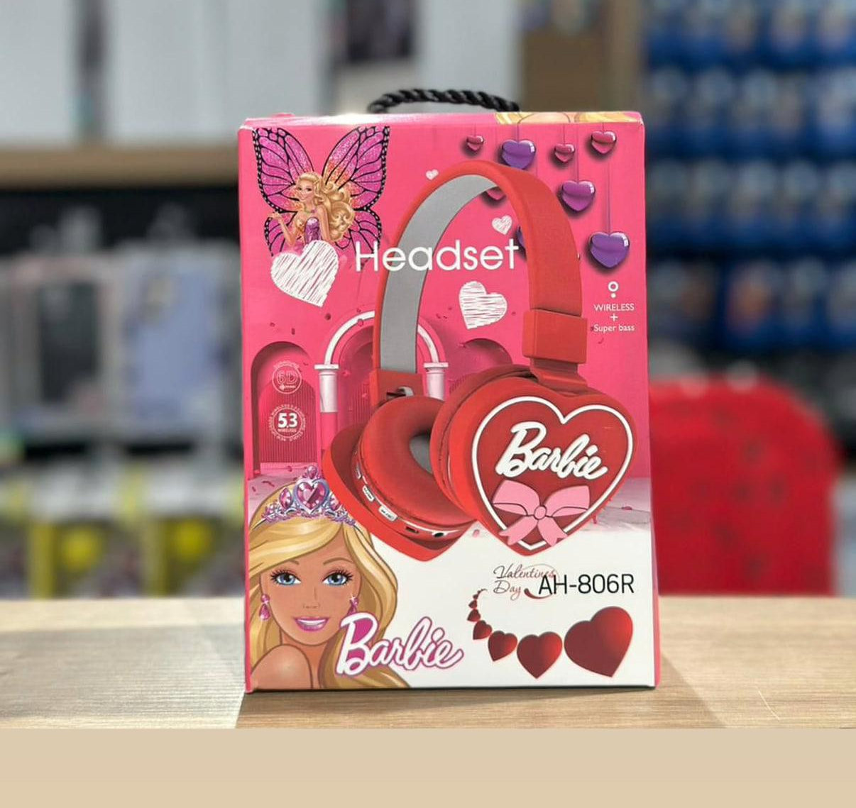 Barbie headset packaging with pink and red design on a blurred store background